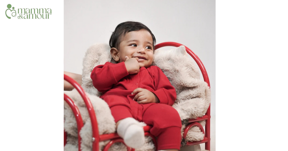 Baby in cherry red organic cotton romper sitting on a red and white chair - Mamma & Amour