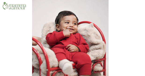 Baby in cherry red organic cotton romper sitting on a red and white chair - Mamma & Amour