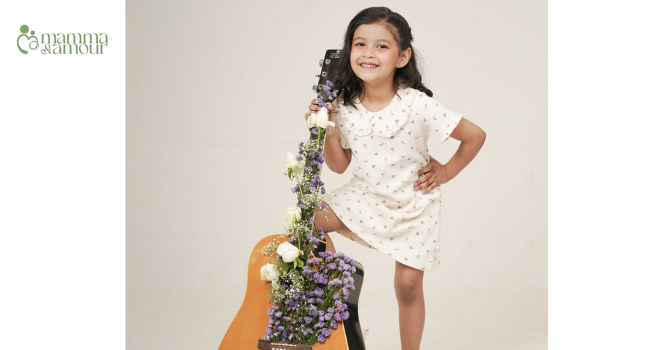 Toddler girl twirling in cherry red frill collared organic cotton dress, garden light in India