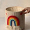 Handwoven macrame nursery storage basket featuring a colorful rainbow and stars for kids room decor.