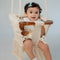 Baby sitting in Mamma & Amour handcrafted macrame and wood baby swing in nursery