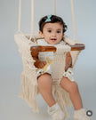 Baby sitting in Mamma & Amour handcrafted macrame and wood baby swing in nursery