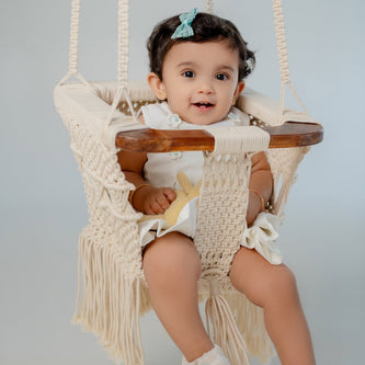 Baby sitting in Mamma & Amour handcrafted macrame and wood baby swing in nursery